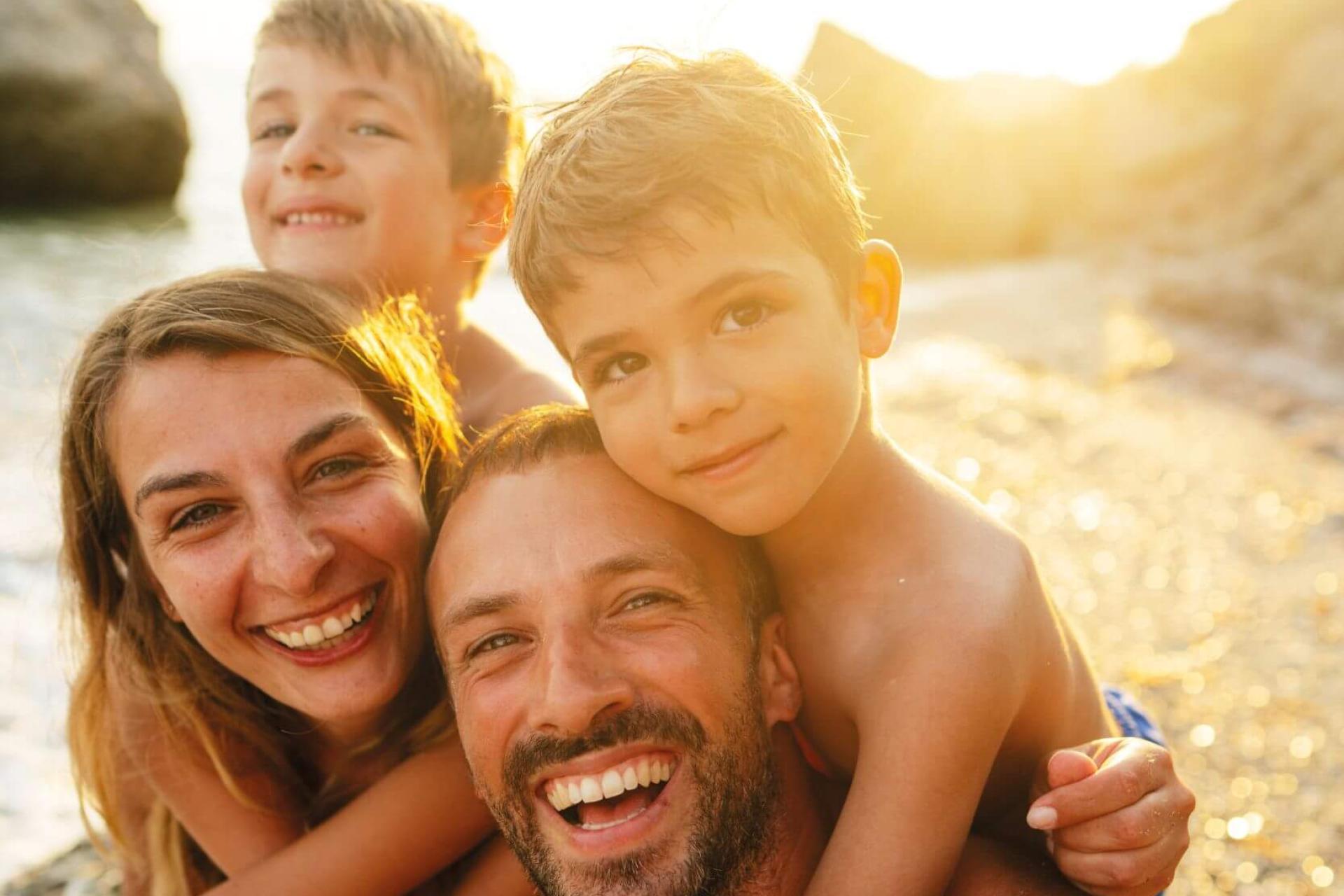 Famiglia felice in spiaggia al tramonto, sorrisi e abbracci.